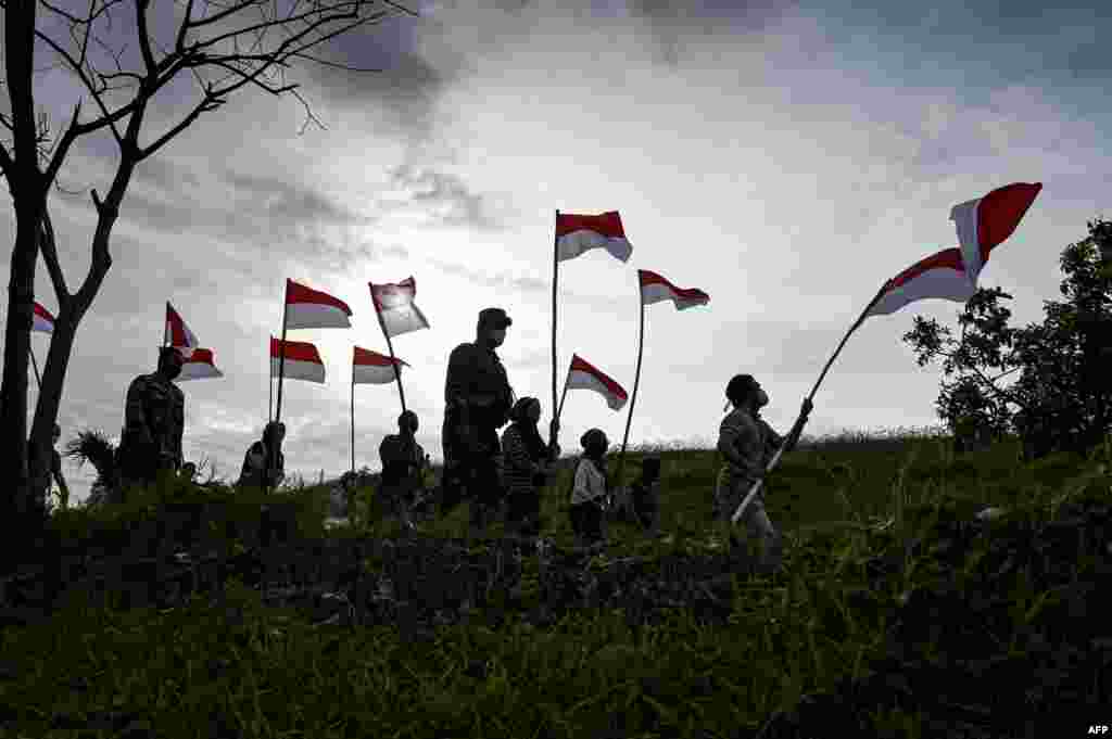 Para pemuda dan remaja membawa bendera Merah-Putih untuk memperingati Hari Kemerdekaan Indonesia ke-76 yang jatuh pada 17 Agustus, di sebuah gunung sampah di Banda Aceh, Senin 16 Agustus 2021. (Foto: Chaidir Mahyuddin / AFP)