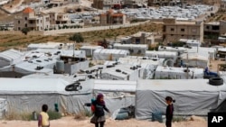 FILE - Syrian refugee children play at an informal refugee camp, which is seen set between the houses and buildings in Arsal, near the border with Syria, east Lebanon, June 13, 2018.