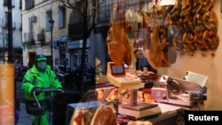 FILE - A municipal worker is seen reflected in a window as he walks past a store selling Iberian ham amid the coronavirus disease (COVID-19) outbreak, in Madrid, Spain, Jan. 22, 2021.