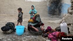 FILE - An internally displaced Afghan woman washes clothes outside her shelter on the outskirts of Kabul, Afghanistan, Feb. 3, 2021. 