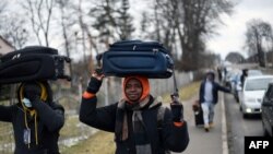 Des hommes fuyant le conflit en Ukraine portent leurs affaires sur leur tête en direction d'un poste frontière entre l'Ukraine et la Pologne, le 28 février 2022.