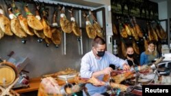 Saleswoman Ainhoa Martinez (R) watches as her chief cuts ham at the Ronda Gourmet shop in downtown Ronda, southern Spain, Sept. 2, 2021.