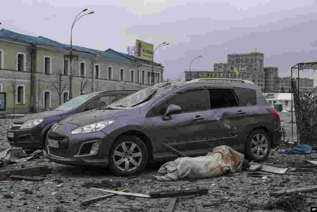 The body of a victim lies next to damaged cars in the central square following shelling of the City Hall building in Kharkiv, March 1, 2022.