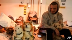 A man sits next to his dogs on mattress in a hotel underground parking turned into a bomb shelter during an air raid alert in Kyiv, Ukraine, Feb. 27, 2022. 