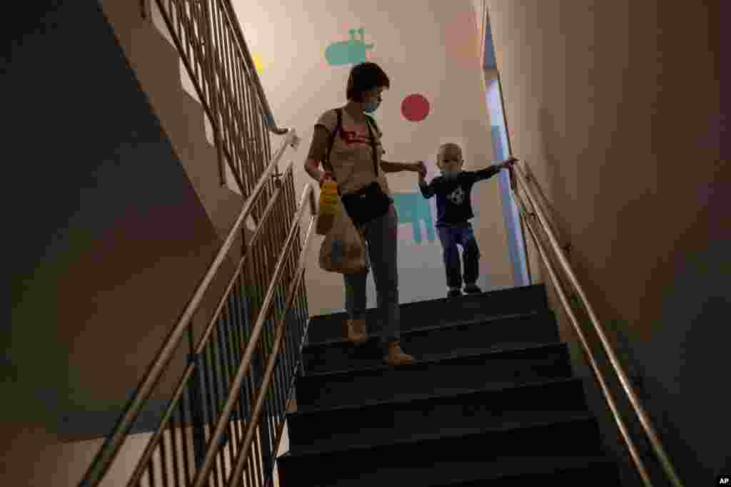 A woman with her son admitted to oncology walks down the stairs to take shelter in a basement used as a bomb shelter, while the sirens sound announcing new attacks, at the Okhmadet children&#39;s hospital in central Kyiv, Ukraine, Feb. 28, 2022.