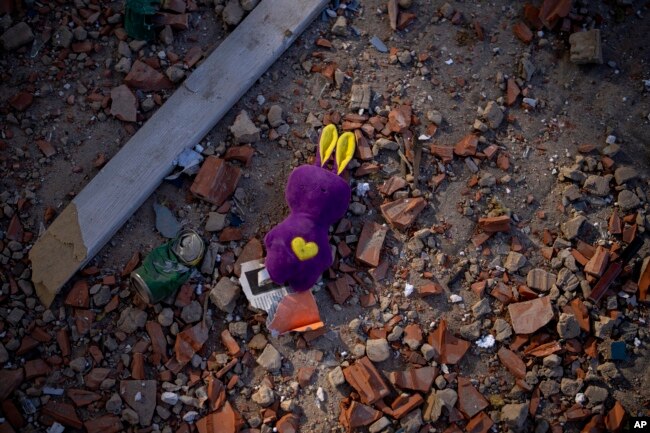 Sebuah mainan tergeletak di antara puing-puing di dekat gedung apartemen yang rusak akibat serangan roket, di Kyiv, Ukraina, Sabtu, 26 Februari 2022. (Foto: AP/Emilio Morenatti)