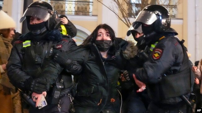 Police officers detain a woman in St. Petersburg, Russia, Feb. 25, 2022. Shocked Russians turned out by the thousands Thursday to protest their country's invasion of Ukraine. Media coverage of the protests has been severely restricted.