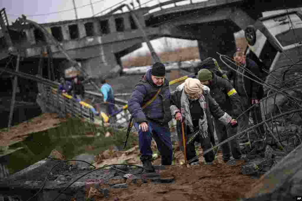Local militiamen help an old woman crossing a bridge destroyed by artillery, as she tries to flee, on the outskirts of Kyiv, Ukraine, March 2. 2022.