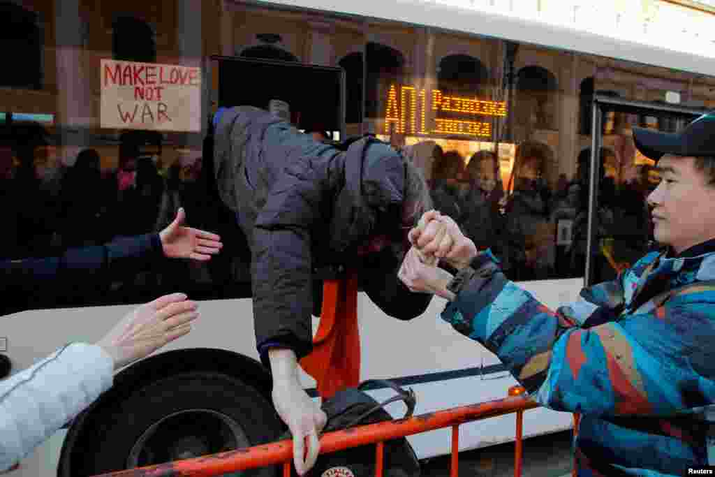 A protester is helped to escape a bus used to transport demonstrators to the police station in Saint Petersburg, Russia, during an anti-war protest against the Russian invasion of Ukraine, Feb. 27, 2022.