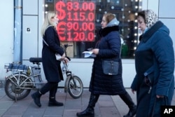 People walk past a currency exchange office screen displaying the exchange rates of U.S. Dollar and Euro to Russian Rubles in Moscow's downtown, Feb. 28, 2022.