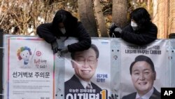 Pejabat dari panitia penyelenggara pemilu memasang poster calon presiden Lee Jae-myung dari Partai Demokrat yang berkuasa dan Yoon Suk Yeol, kanan, dari oposisi utama People Power Party di Seoul, Korea Selatan, 18 Februari 2022. (Foto: titik)