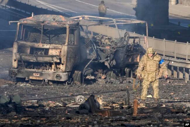 A Ukrainian soldier walks past debris of a burning military truck, on a street in Kyiv, Ukraine, Feb. 26, 2022.