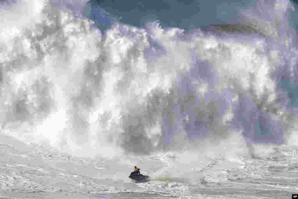 A jet ski moves away from a crashing wave during a big wave surfing session at Praia do Norte, or North Beach, in Nazare, Portugal.