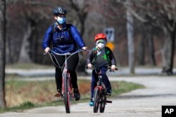 In this April 8, 2020, photo, bicyclists wear pandemic masks while riding in Portland, Maine.