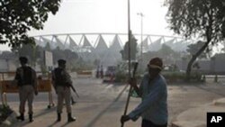 A sweeper cleans the surroundings as security guards stand guard outside the Jawaharlal Nehru stadium, the main venue of the Commonwealth Games early in the morning in New Delhi, India, 26 Sept. 2010.
