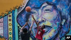 Jamari Baugh bermain bola basket bersama temannya di sebelah mural pengaran Zora Neale Hurston, yang besar di Eatonville, yang kerap menggambarkan kota fiksi warga kulit hitam bersejarah dalam karyanya, di Eatonville, Florida, 23 Agustus 2023. (Foto: Rebecca/Blackwell/AP Photo)