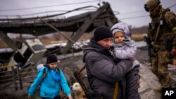 Anggota milisi lokal Valery, 37, membantu sebuah keluarga yang melarikan diri di sepanjang jembatan yang dihancurkan oleh tembakan artileri, 2 Maret 2022, di luar Kyiv, Ukraina. (Foto: AP)