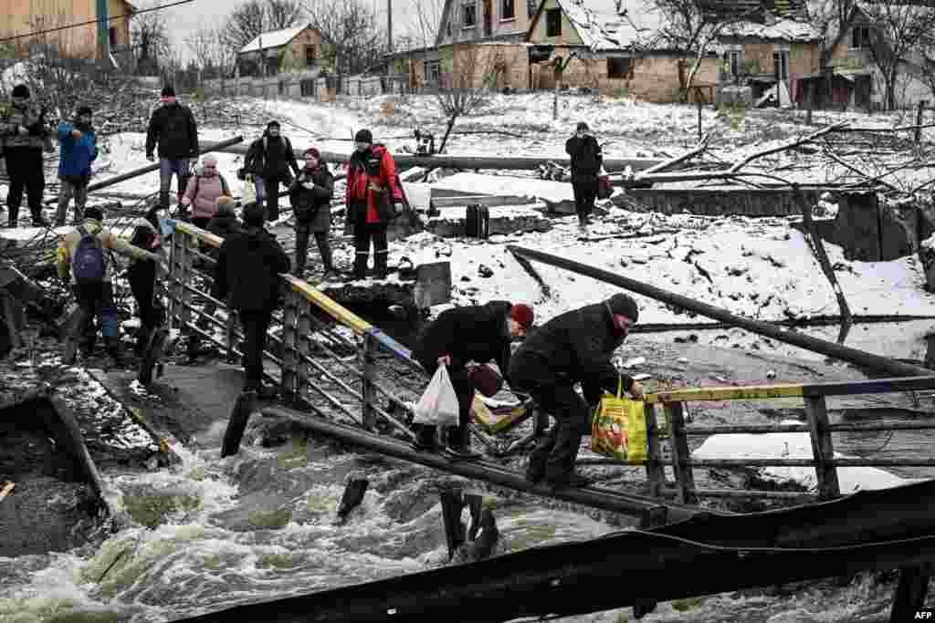 Civilians attempt to cross a bridge that was blown up by Russian forces in the north of Kyiv, Ukraine.