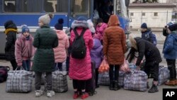 Children wait by bags with their belongings as they arrive at a train station to leave Kostiantynivka, Donetsk region, eastern Ukraine, Feb. 24, 2022.