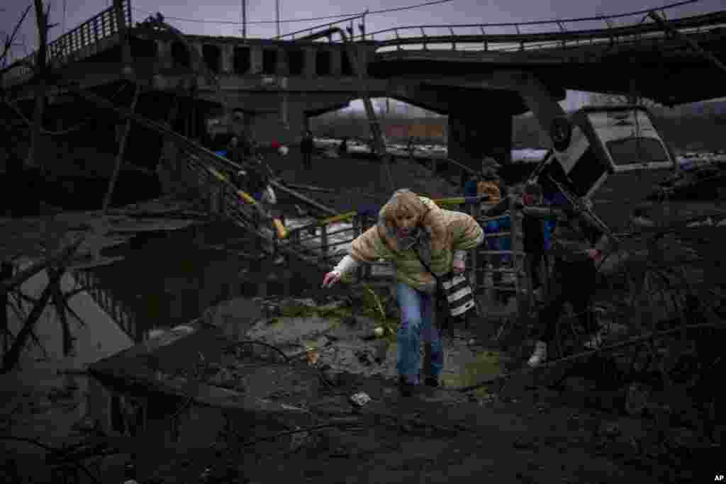 A woman flees with her family crosses a destroyed bridge in the outskirts of Kyiv, Ukraine.