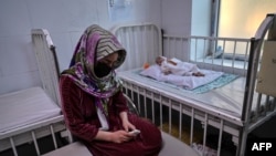 FILE - A woman sits next to her baby, who is being treated for malnutrition at a Doctors Without Borders nutrition center in Herat, Afghanistan, Nov. 22, 2021.