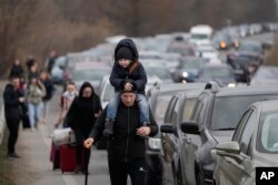 Pengungsi Ukraina berjalan di sepanjang kendaraan yang berbaris untuk menyeberangi perbatasan dari Ukraina ke Moldova, di titik perbatasan persimpangan Mayaky-Udobne dekat Mayaky-Udobne, Ukraina, Sabtu, 26 Februari 2022. (Foto: AP)