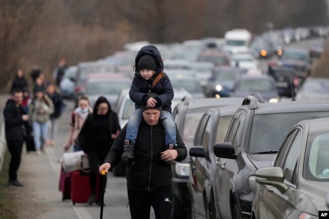 Pengungsi Ukraina berjalan di sepanjang kendaraan yang berbaris untuk menyeberangi perbatasan dari Ukraina ke Moldova, di titik perbatasan persimpangan Mayaky-Udobne dekat Mayaky-Udobne, Ukraina, Sabtu, 26 Februari 2022. (Foto: AP)