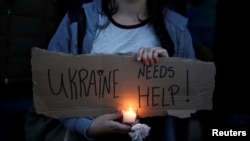 一位抗议者手里举着纸牌，上面写着“乌克兰需要帮助！”