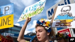 Seorang perempuan Ukraina mengacungkan poster dalam demo memprotes invasi Rusia ke Ukraina, di Los Angeles, AS, Sabtu, 26 Februari 2022. (Foto: Richard Voge/AP)