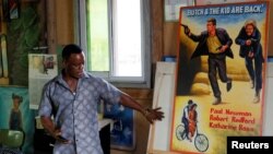 Ghanaian movie poster artist, Daniel Anum Jasper, 54, stands next to a hand-painted poster commissioned for a foreign client at his workshop in the Teshie area of Accra, Ghana February 20, 2022. (REUTERS/Francis Kokoroko)