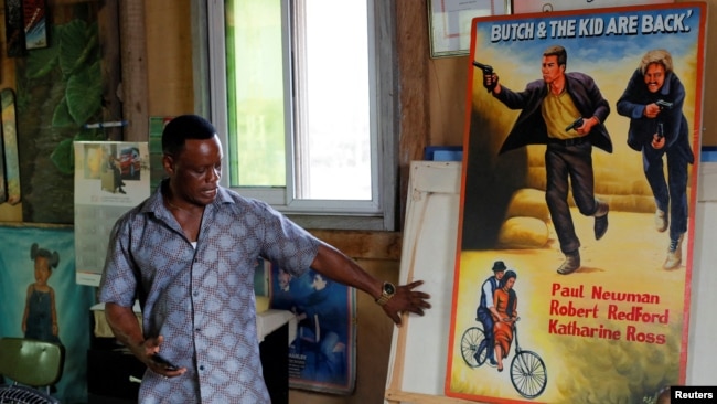 Ghanaian movie poster artist, Daniel Anum Jasper, 54, stands next to a hand-painted poster commissioned for a foreign client at his workshop in the Teshie area of Accra, Ghana February 20, 2022. (REUTERS/Francis Kokoroko)