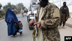 FILE - A burqa-clad woman and a child walk past Taliban fighters along a roadside in Jalalabad, Afghanistan, Dec. 12, 2021.