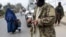 FILE - A burqa-clad woman and a child walk past Taliban fighters along a roadside in Jalalabad, Afghanistan, Dec. 12, 2021.