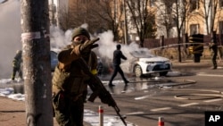 Ukrainian soldiers take positions outside a military facility as two cars burn, in a street in Kyiv, Ukraine, Saturday, Feb. 26, 2022. Russian troops stormed toward Ukraine's capital Saturday. (AP Photo/Emilio Morenatti)