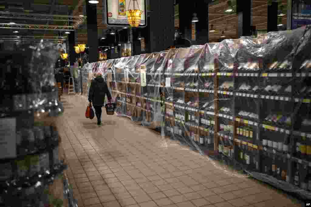 A customer walks past plastic-covered shelves with alcoholic beverages that have been banned for sale at a supermarket in Kyiv, Ukraine.
