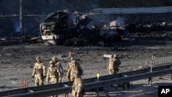 Soldados ucranianos passam por destroços de um camião militar em chamas numa rua em Kyiv, Ucrânia, 26 de Fev. 2022. Tropas russas invadiram a capital da Ucrânia no sábado, e os combates de rua eclodiram.