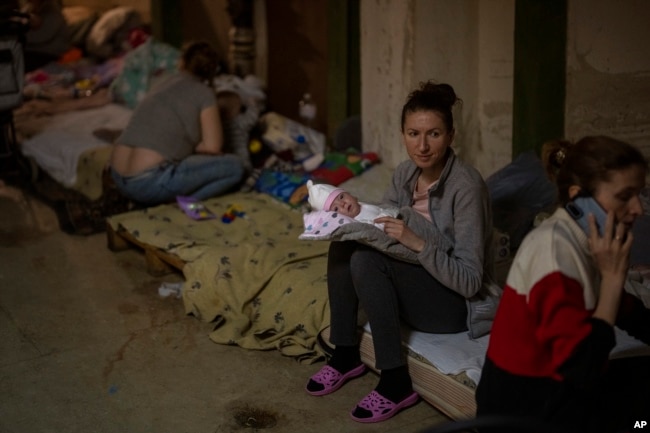 A woman holds her newborn baby at a basement used as a bomb shelter at the Okhmadet children's hospital in central Kyiv, Ukraine, Feb. 28, 2022. (AP Photo/Emilio Morenatti)