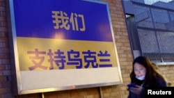 A woman on her cellphone walks past a billboard in support of Ukraine following Russia's invasion of the country, where graffiti is covered up, in Beijing, China, March 2, 2022.