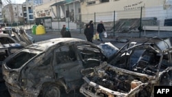 People walk near cars that were destroyed by recent shelling on the outskirts of Kyiv, Feb. 28, 2022. 