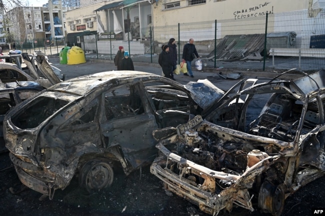 People walk near cars that were destroyed by recent shelling on the outskirts of Kyiv, Feb. 28, 2022. (Photo by Genya SAVILOV / AFP)