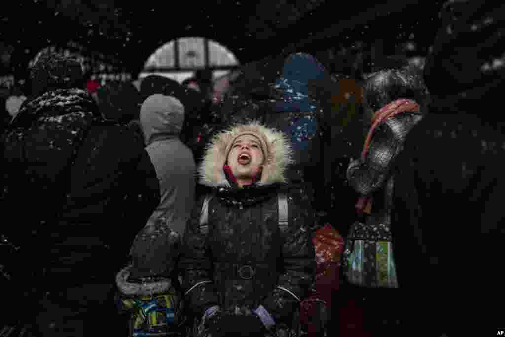 Una niña atrapa copos de nieve mientras espera con otros para abordar un tren a Polonia, en la estación de tren de Lviv, el domingo 27 de febrero de 2022, en Lviv, Ucrania occidental. (Foto AP/Bernat Armangue)