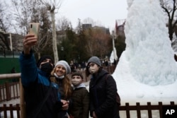 Orang-orang berpose dengan air mancur beku di sebuah taman di Ankara, Turki, Kamis, 3 Februari 2022. (AP/Burhan Ozbilici)