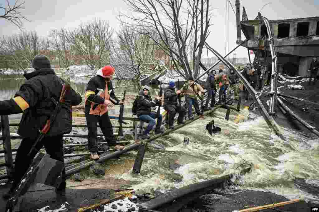 Members of an Ukrainian civil defense unit pass new assault rifles to the opposite side of a blown up bridge on Kyiv&#39;s northern front, March 1, 2022.