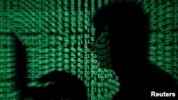 FILE - A man works on a computer as cyber code is projected on him in this illustration created on May 13, 2017. A new report says Kenya is experiencing an increase in online sexual exploitation and abuse of children. 