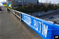 Victor Chepras, yang berasal dari Ukraina, mengibarkan bendera Ukraina, 1 Maret 2022, di dekat papan bertuliskan 'Stop Putin.' (Foto: AP)