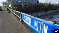 Victor Chepras, who is from Ukraine, waves Ukrainian flags, March 1, 2022, near a sign that reads 'Stop Putin,' over Interstate 5 in Seattle near the University of Washington, in protest against Russia's invasion of Ukraine. 
