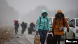 People fleeing Russia's military operation against Ukraine walk toward the Shehyni border crossing to Poland past cars waiting in line to cross the border, outside Mostyska, Ukraine, Feb. 27, 2022.