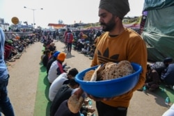 Orang-orang makan siang di dapur komunitas di dekat barikade saat para petani melancarkan aksi protes reformasi pertanian baru-baru ini, di perbatasan negara bagian Delhi-Haryana di Singhu, 14 Desember 2020. (Foto: Prakash SINGH / AFP)