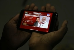 A man in Hyderabad, India watches on his mobile phone Prime Minister Narendra Modi address the nation in a televised speech about COVID-19 situation, April 14, 2020.