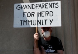 FILE - A demonstrator holds a sign reading "Grandparents for Herd Immunity" as protestors rally against COVID-19 restrictions outside the Pennsylvania State Capitol Building in Harrisburg, Pennsylvania, U.S., May 15, 2020.